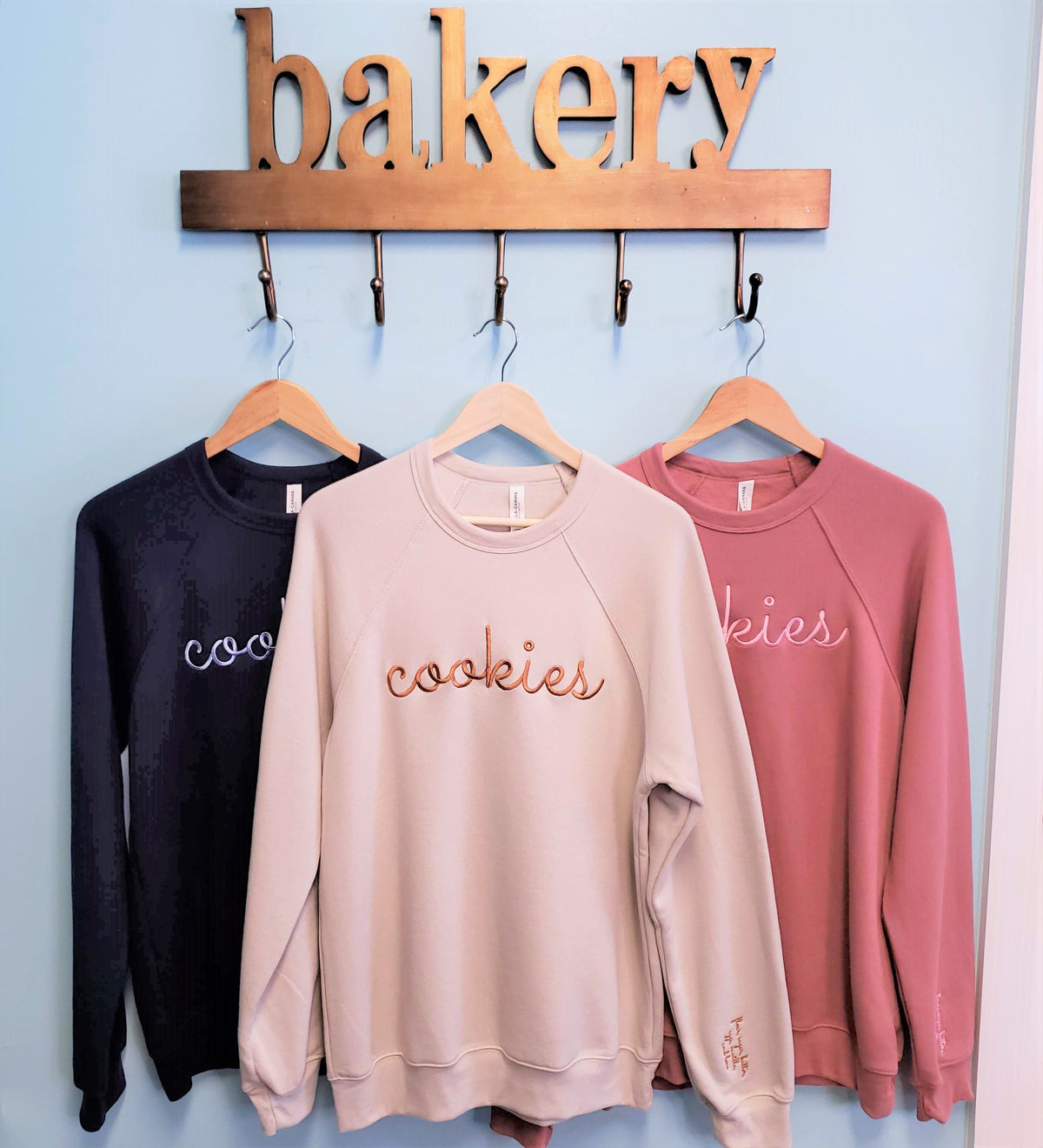 A soft blush-colored long-sleeved sweatshirt with cookies embroidered in rose-gold thread across the chest