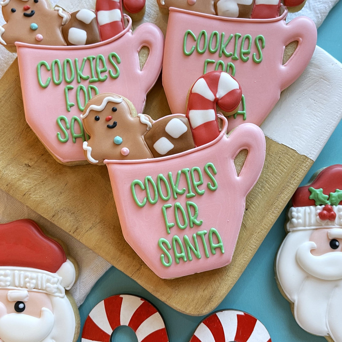 Pink frosted cookie shaped like a mug with green icing text cookies for santa decorated with gingerbread man marshmallows and candy canes from cookies for santa cutter bundle