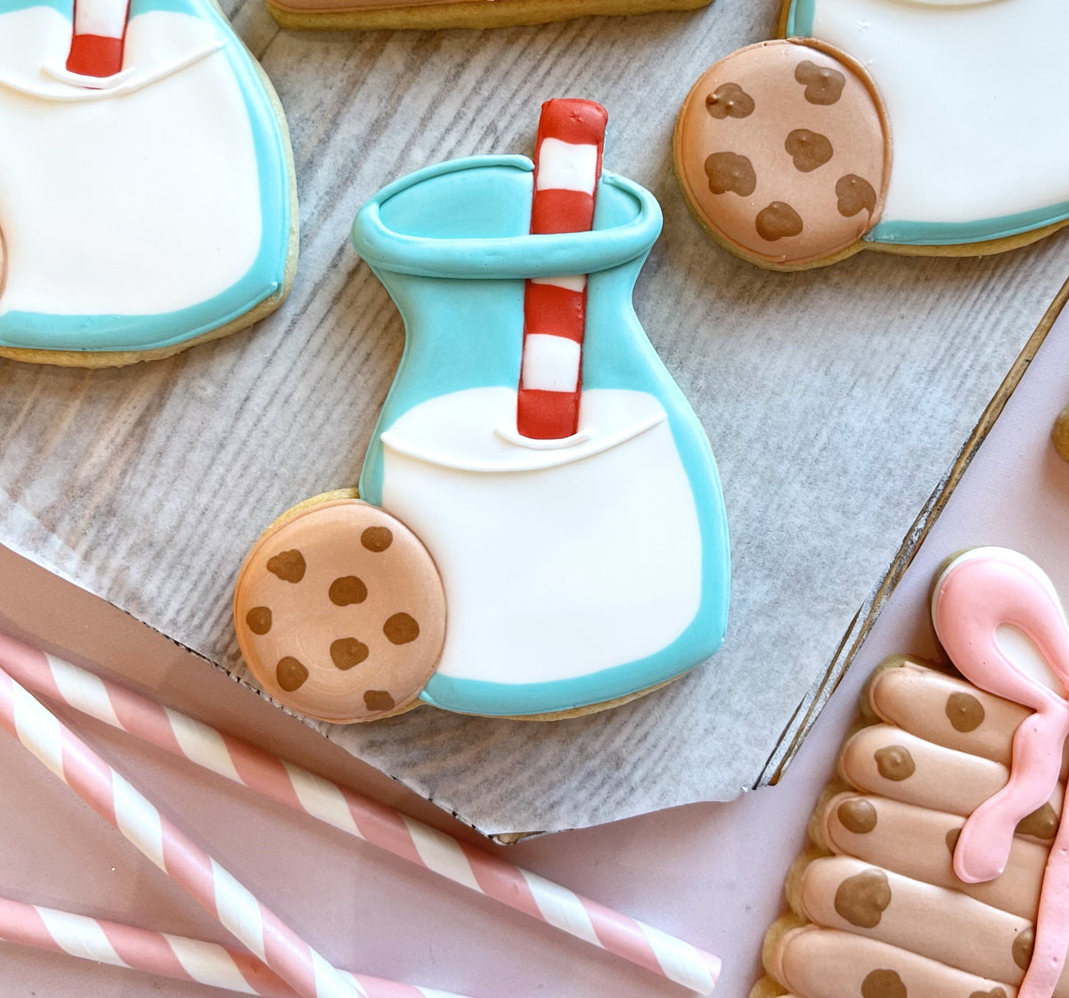 A light blue frosted milk bottle cookie with white icing and red striped straw next to a chocolate chip cookie from the cookies for Santa cutter bundle