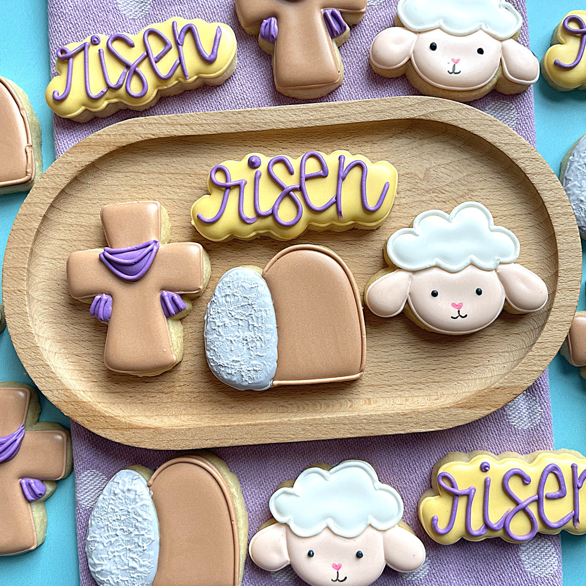Easter themed sugar cookies shaped like crosses eggs and sheep with purple icing on wooden tray made with mini empty tomb cookie cutter