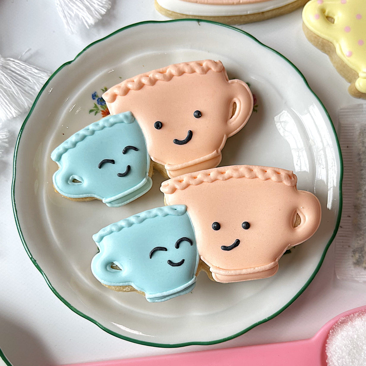 Pastel blue and peach sugar cookies shaped like smiling teacups made with mini snuggling teacups cookie cutter on white plate