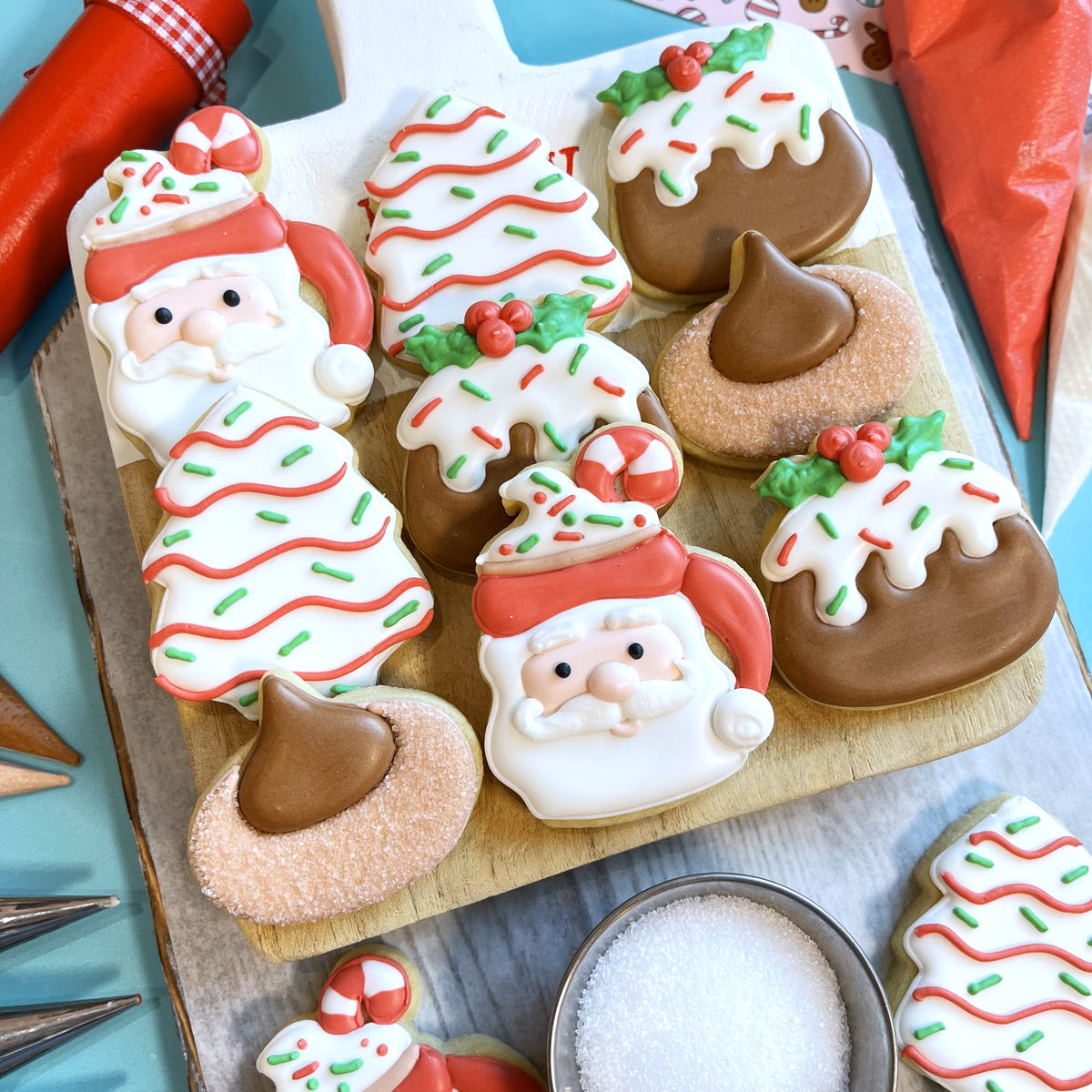 Mini pb blossom cookie cutter sugar cookies decorated with santa claus trees white icing red lines green sprinkles and chocolate drizzle