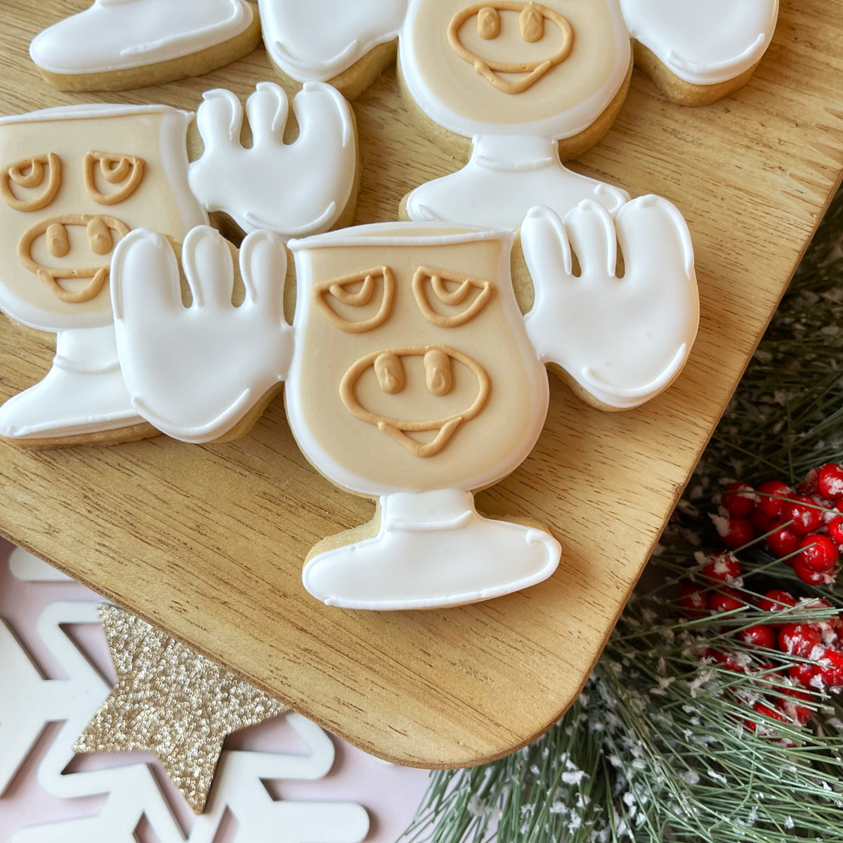 Delicate ghost-shaped sugar cookies with white icing and beige details arranged on a wooden board from christmas movie 2.0 cookie cutter bundle