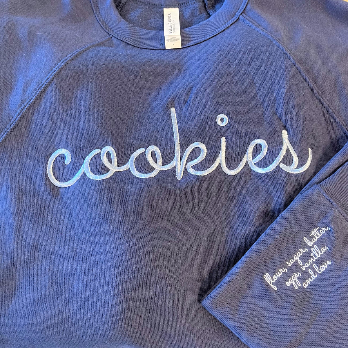 Navy blue sweatshirt with cookies embroidered in white cursive script on chest and sleeve ingredients text