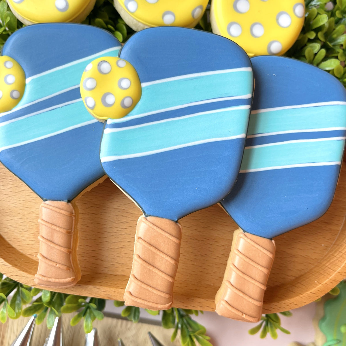Blue and light blue striped pickleball paddle cookie cutter cookies with tan handles and yellow polka dot balls