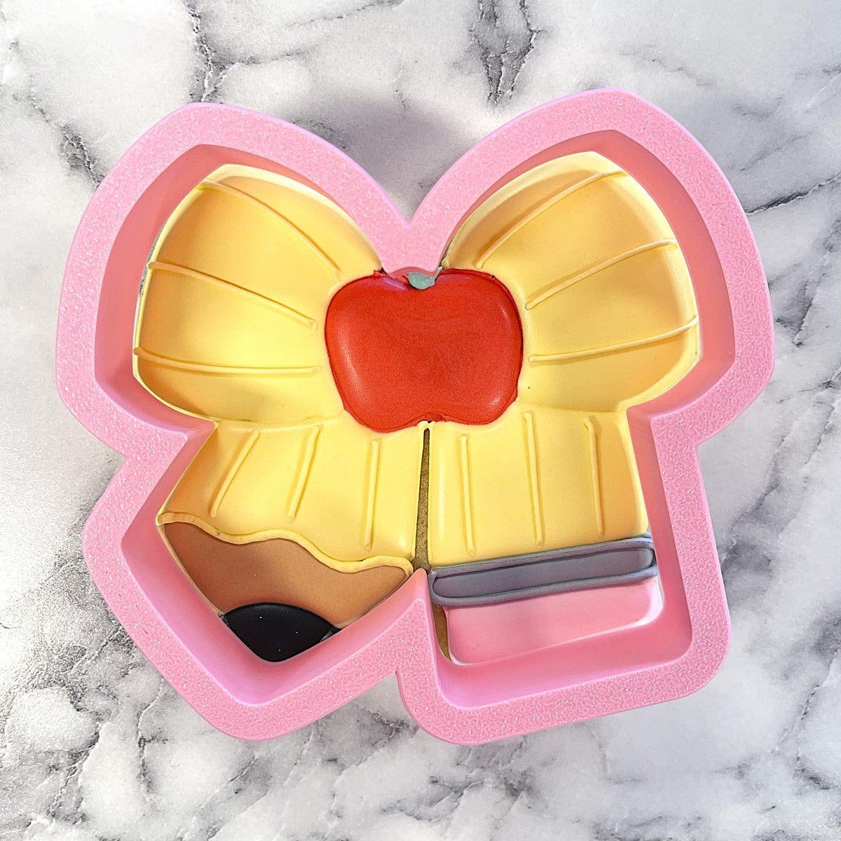 Pink silicone pencil bow cookie cutter with yellow bow and red apple detail for baking and crafting use