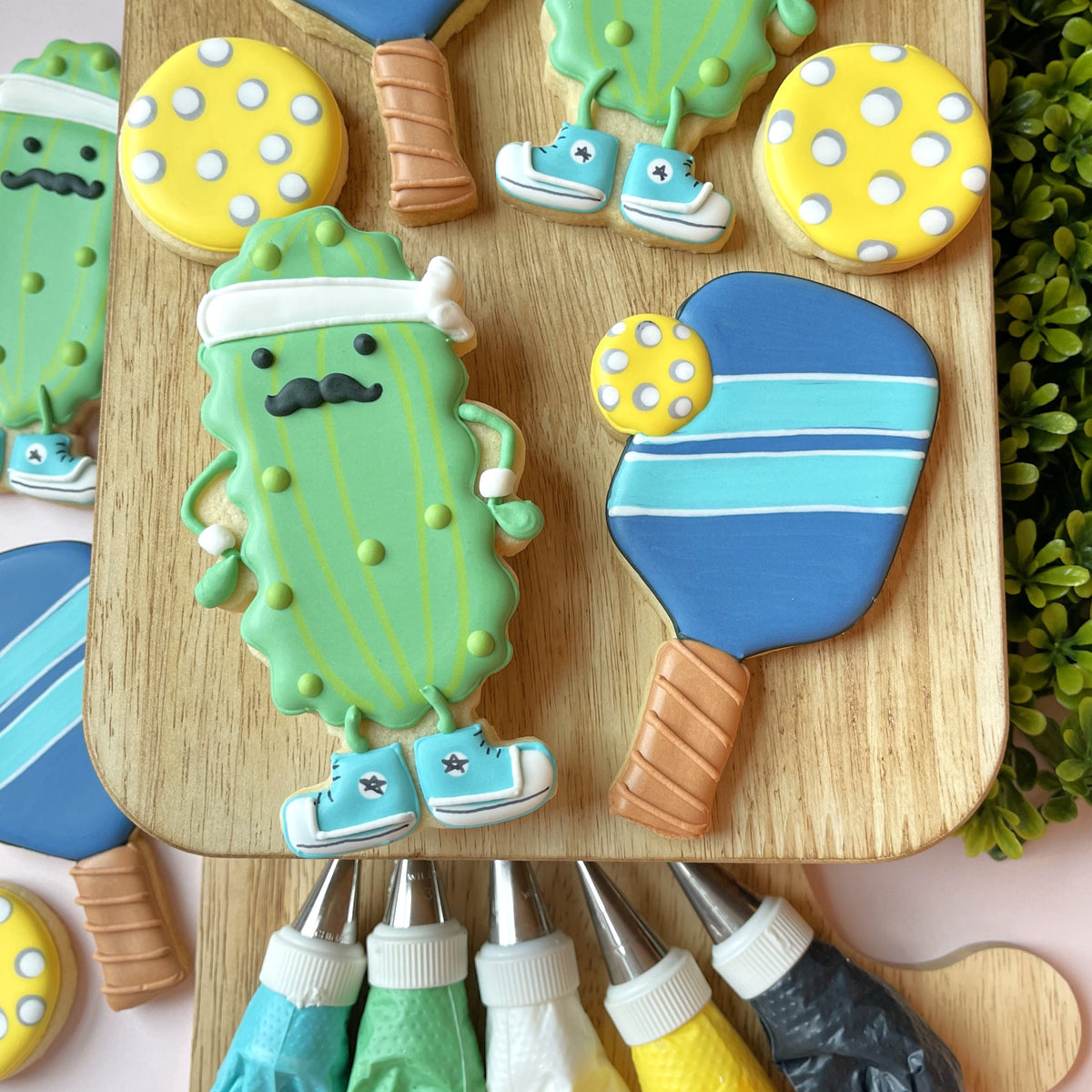 A green pickle-shaped cookie with a white headband black mustache and blue sneakers from a pickleball cookie cutter bundle