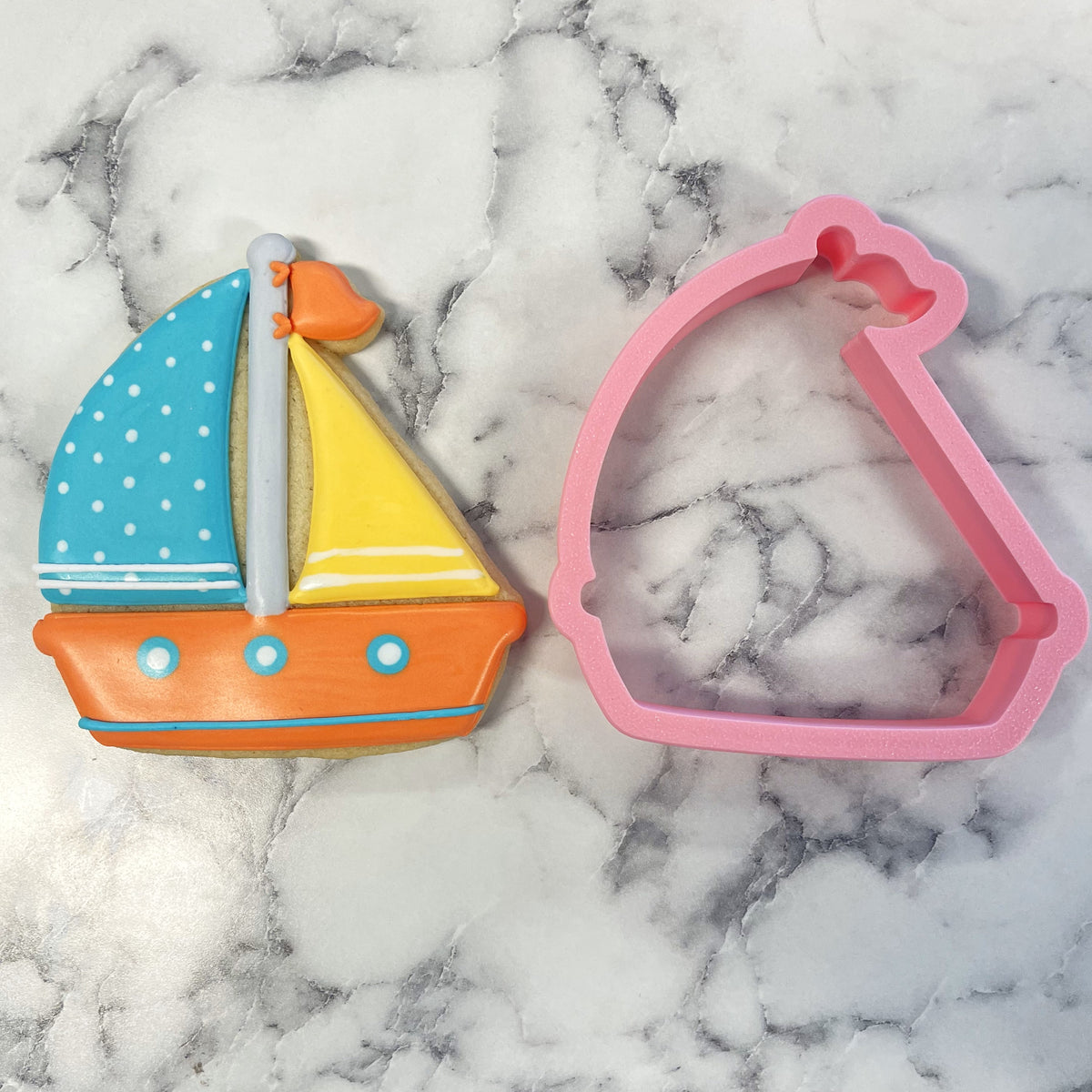Colorful sugar cookie shaped like a sailboat with blue and yellow sails orange hull and white polka dots made using sailboat cookie cutter