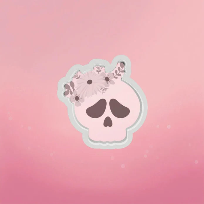 A pink skull cookie cutter with delicate floral designs and a light gray border for decorative baking