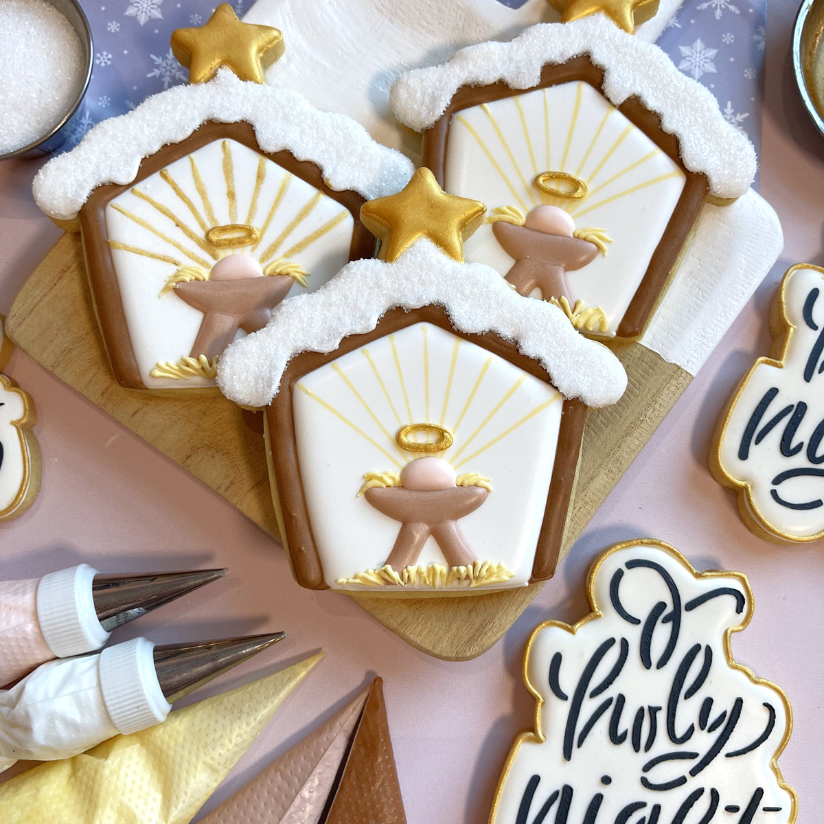 Delicate white and brown sugar cookies shaped like nativity scenes with gold star toppers made using snowy stable cookie cutter