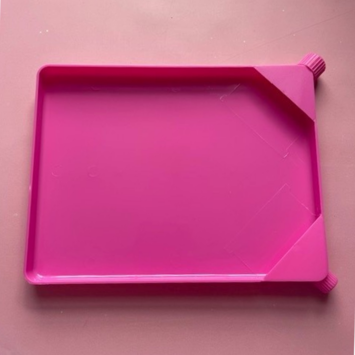 Bright pink plastic sprinkle tray with raised edge and two small corner knobs for easy handling