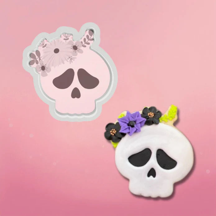 White skull-shaped cookie cutter with black eye sockets and a purple and black floral crown design