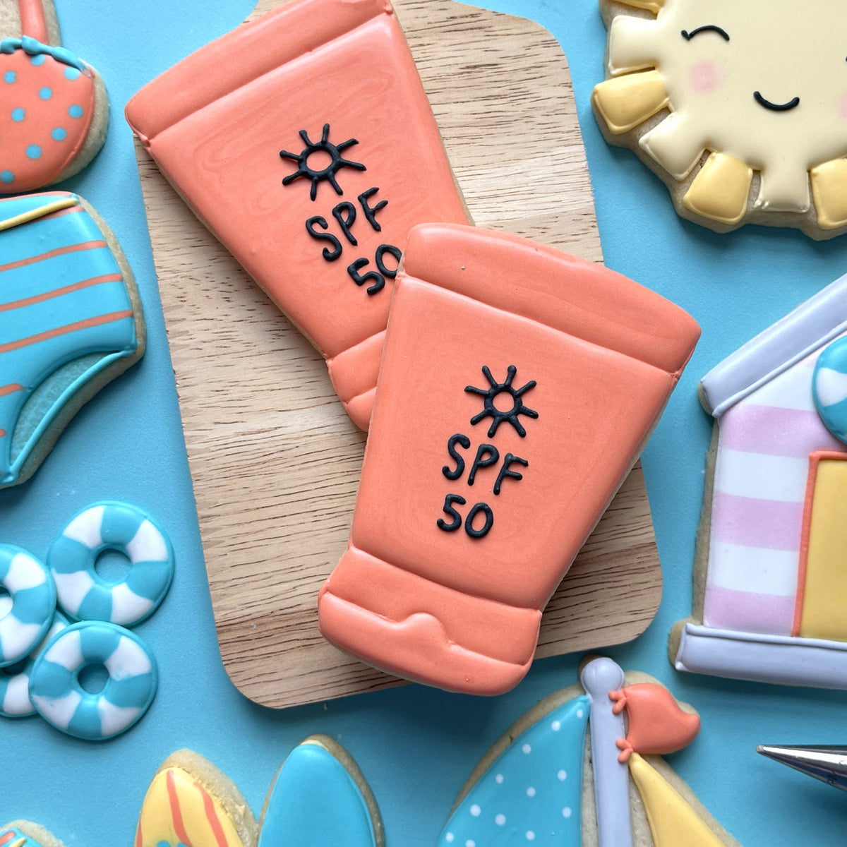 Coral-colored sugar cookie shaped like an spf 50 sunscreen tube with black icing details using sunscreen cookie cutter
