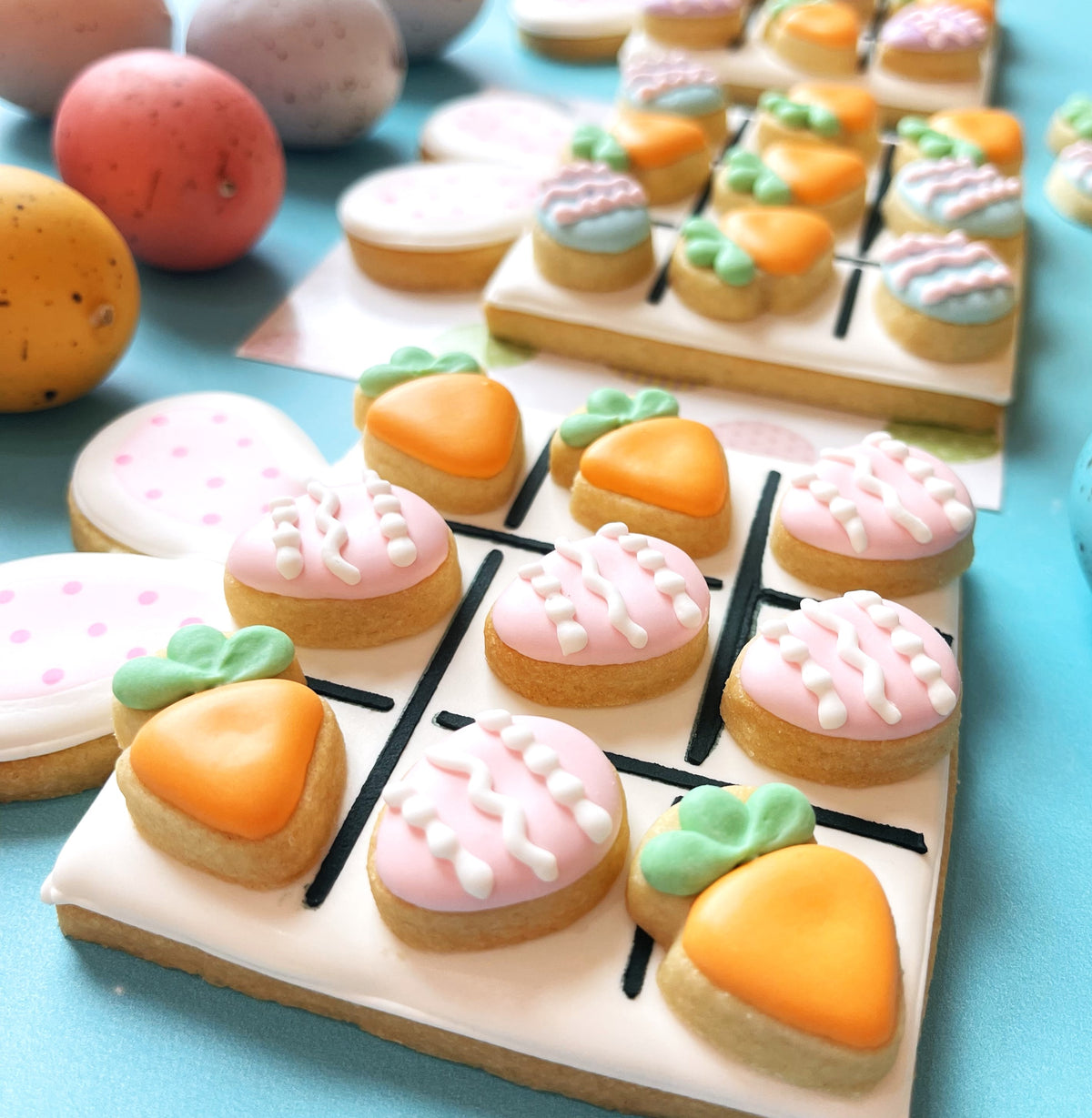 Pastel-colored carrot-shaped cookies with pink and orange icing made using tic tac toe bunny card cookie cutter set