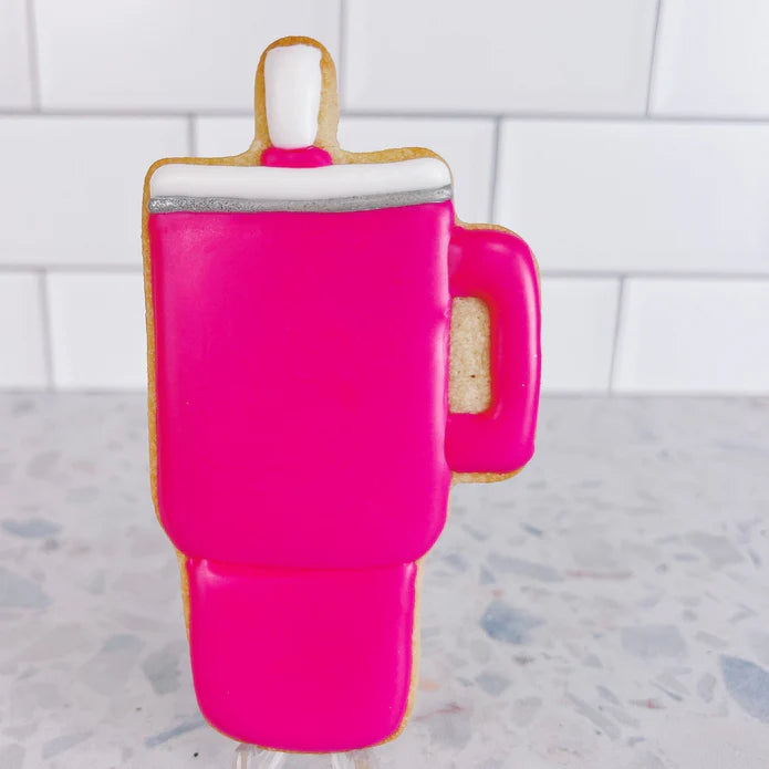 A vibrant pink frosted cookie shaped like a mug with a white and silver rim made using trendy tumbler cookie cutter