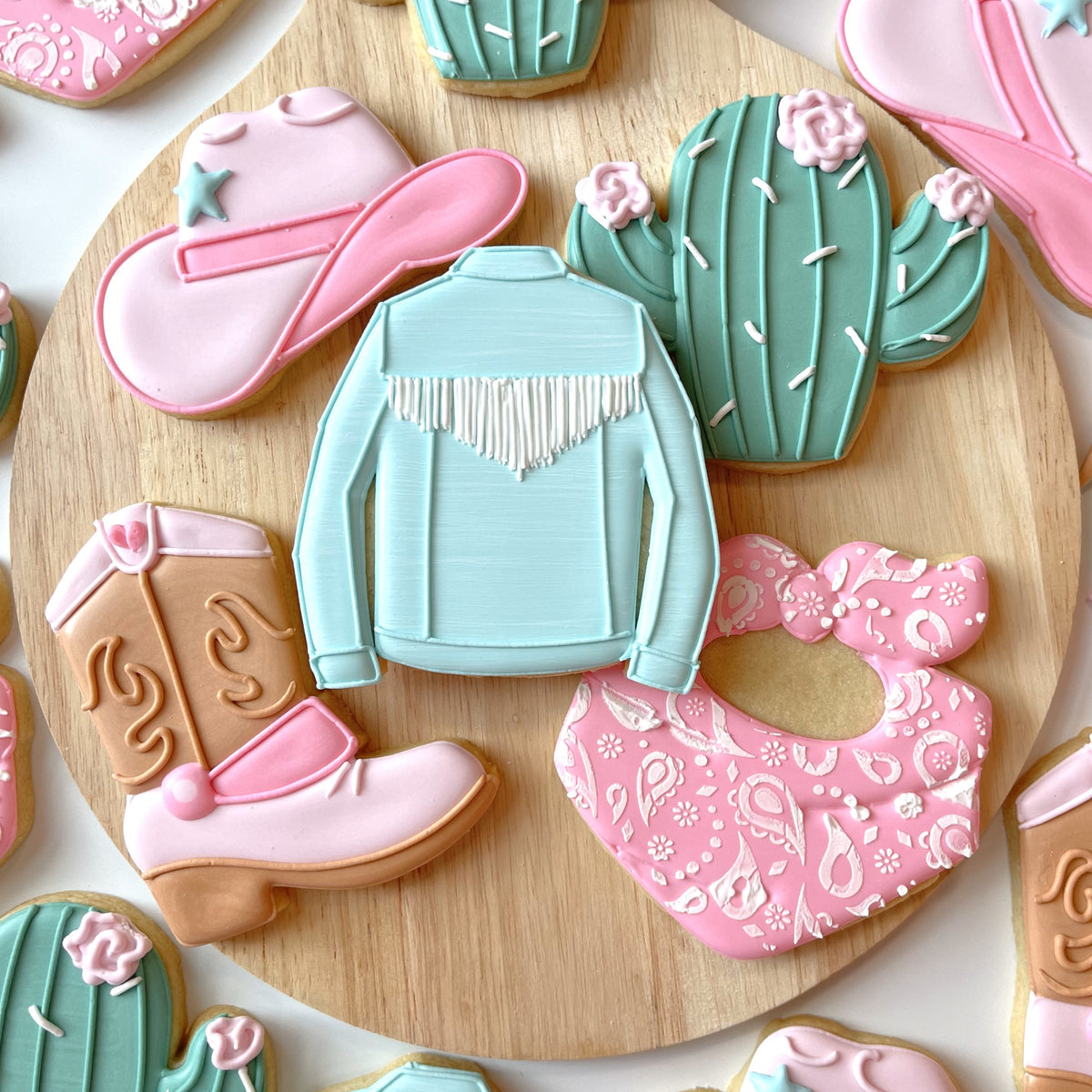 Pastel blue sugar cookie shaped like a western-style jacket with white fringe made using western boot cookie cutter