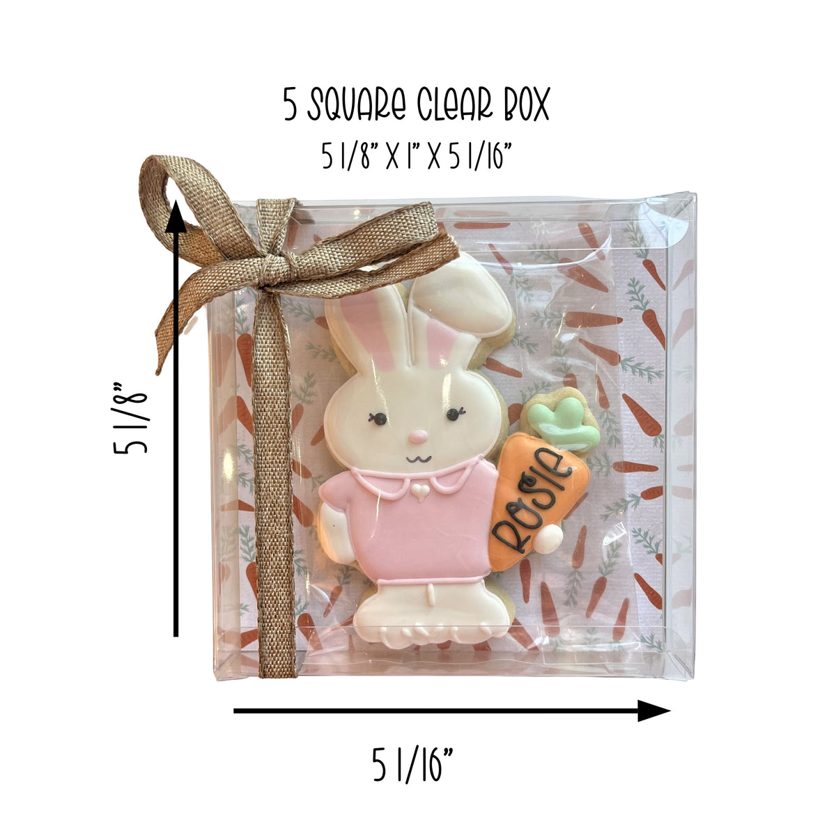 A pink and white bunny sugar cookie holding a carrot in a 5 1/8 by 1 by 5 1/16 inch clear square cookie box with brown ribbon