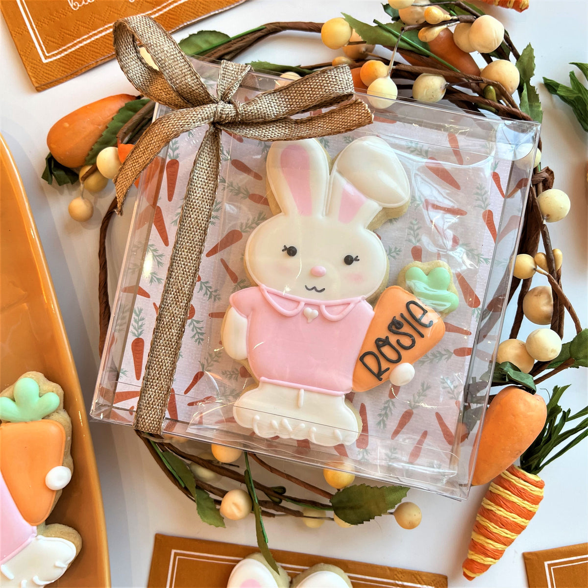 A pink and white bunny-shaped cookie in a 5 inch square clear plastic gift box tied with a brown ribbon