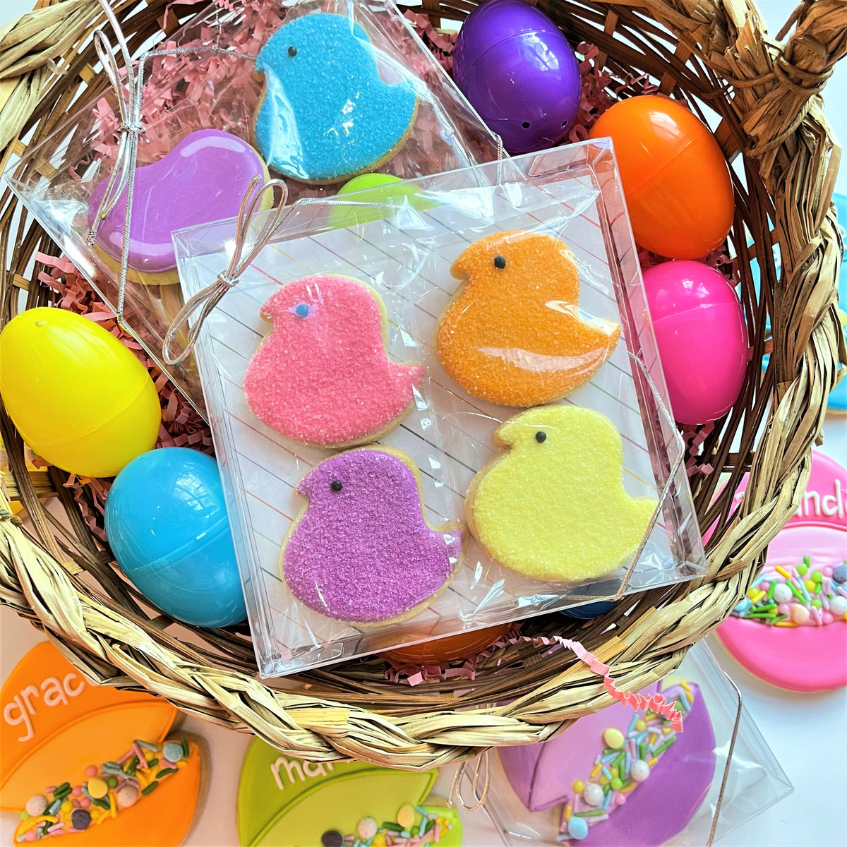 A clear plastic 5 inch square cookie box containing four colorful sugar coated chick shaped cookies packaged for sale