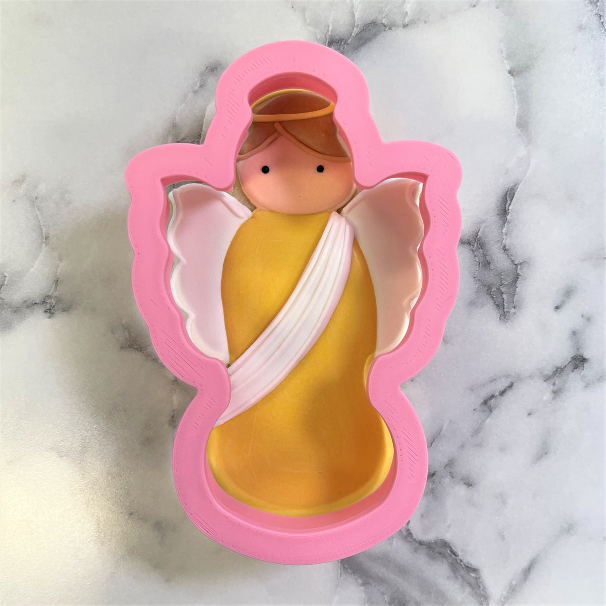 Pink silicone Christmas angel cookie cutter with yellow and white icing details for festive holiday baking