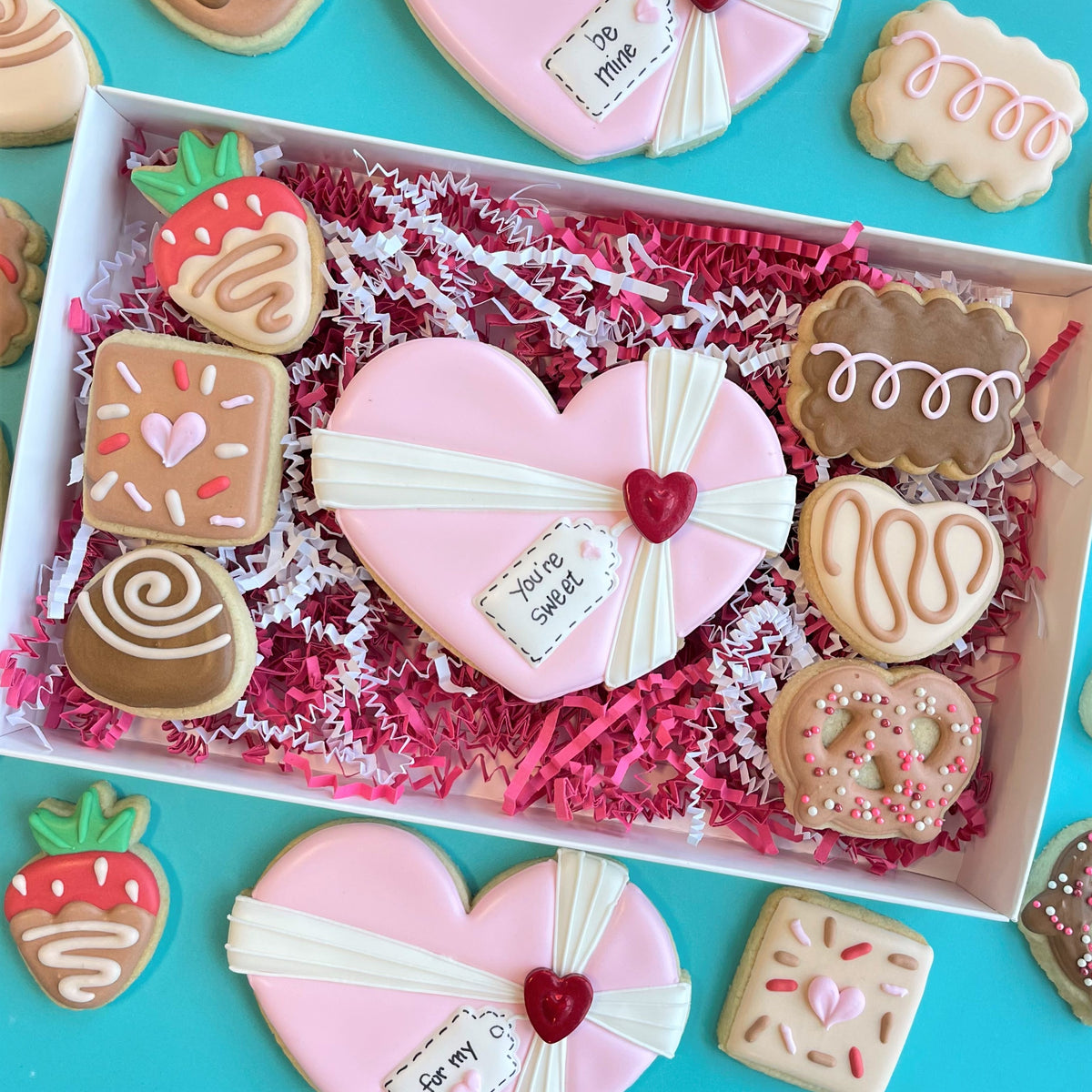 Pink heart-shaped cookie decorated with white icing ribbon and red heart charm from chocolate heart box cookie cutter set