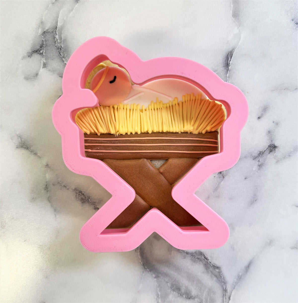 Pink silicone baby jesus cookie cutter mold featuring a sleeping baby in a manger with straw and wooden details