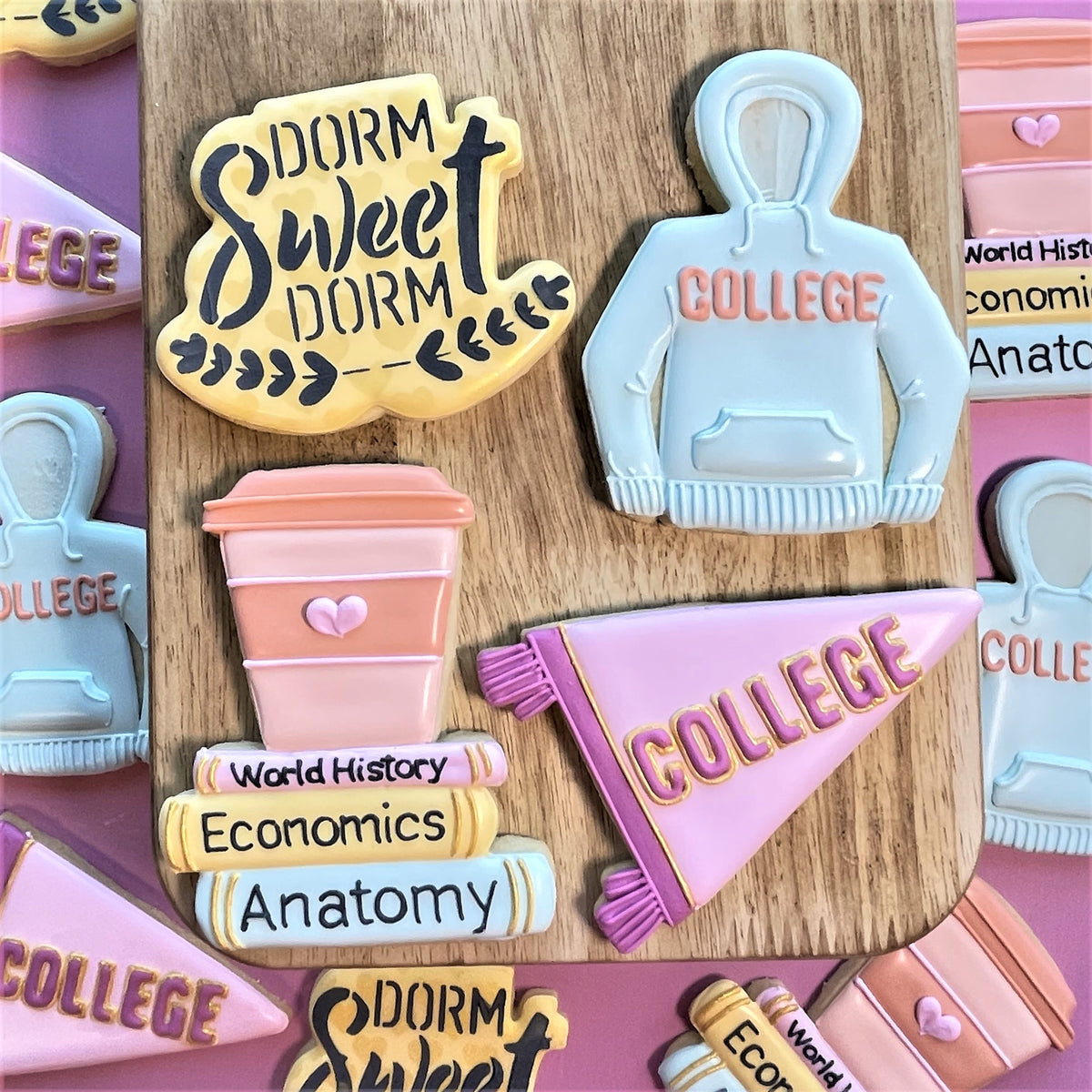 Pastel blue hoodie-shaped cookie with peach college lettering made using dorm sweet dorm plaque cookie cutter with stencil