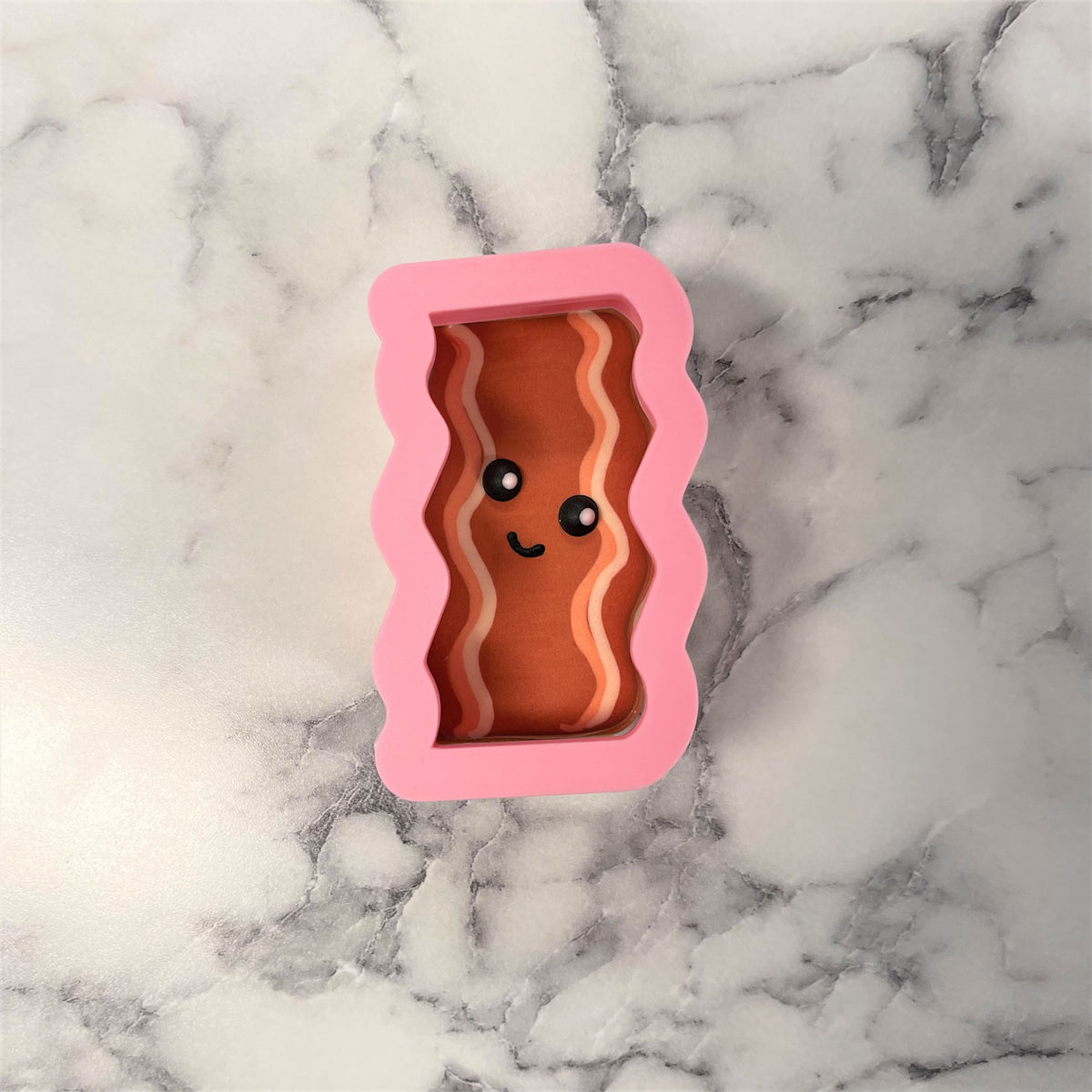 Pink silicone bacon-shaped cookie cutter with smiling face design for baking and crafting use