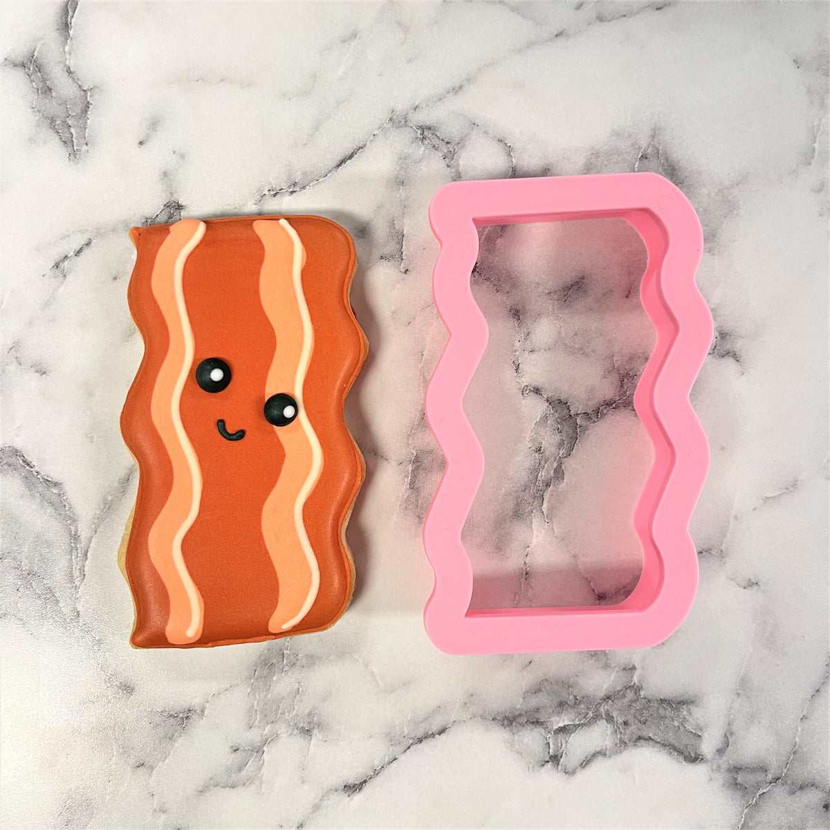 Cute orange bacon cookie cutter with smiling face and white stripes paired with matching pink silicone mold for baking
