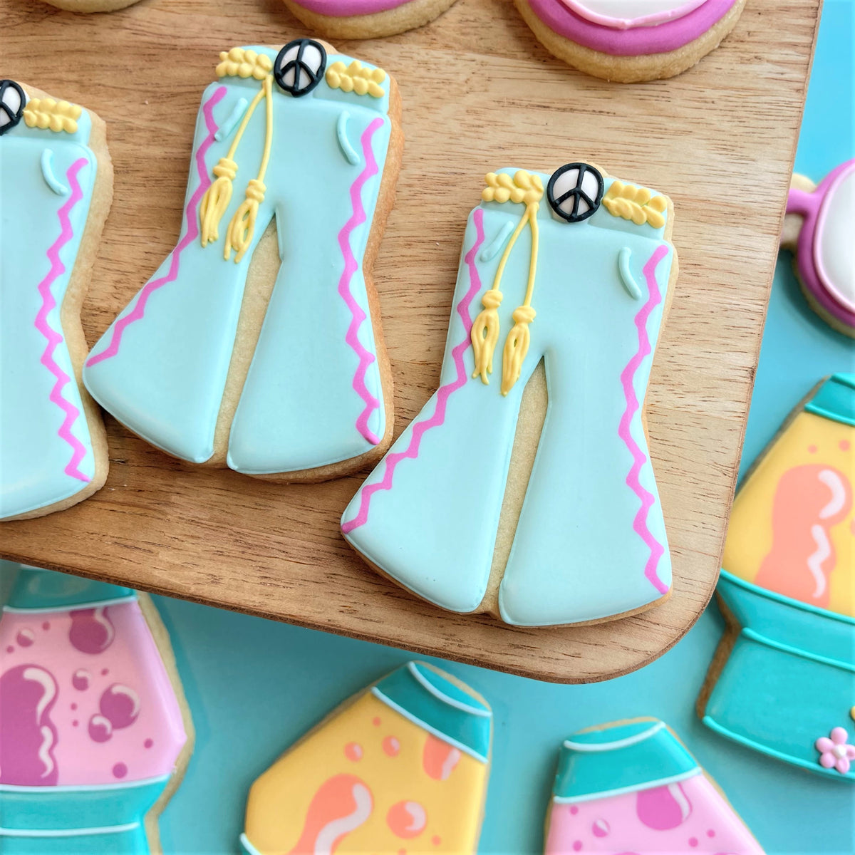 Light blue sugar cookies shaped like bell-bottom pants with pink zigzag icing and yellow tassels from groovy 5 cutter bundle