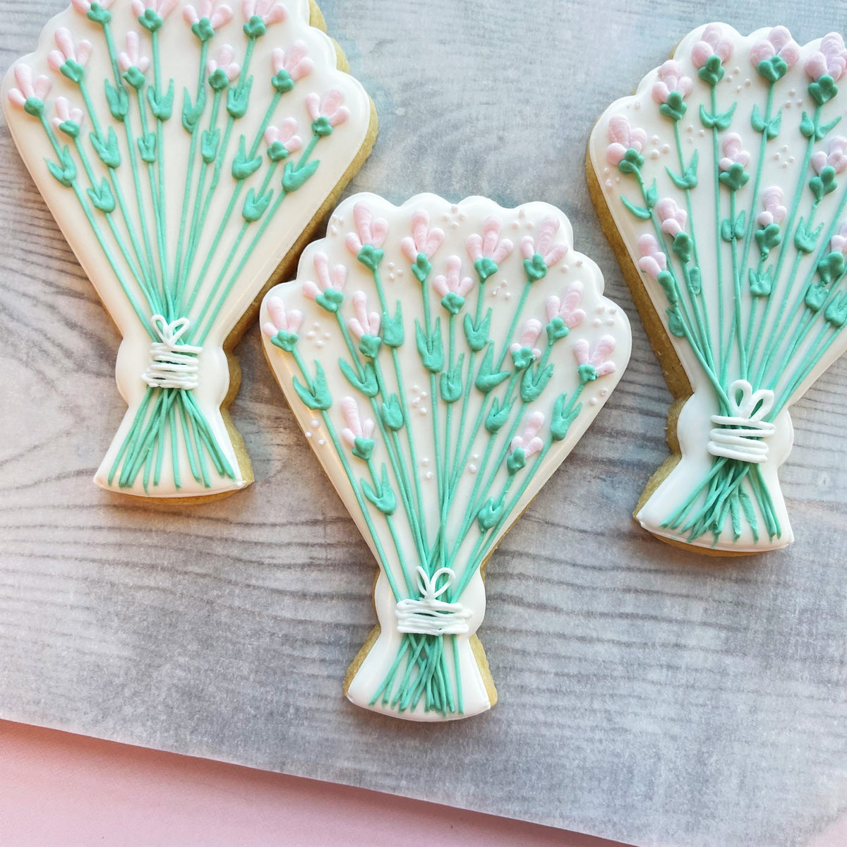 Delicate lavender bouquet-shaped sugar cookies with pink and mint green icing tied with white fondant bow for rustic wedding cookie decorating class recording