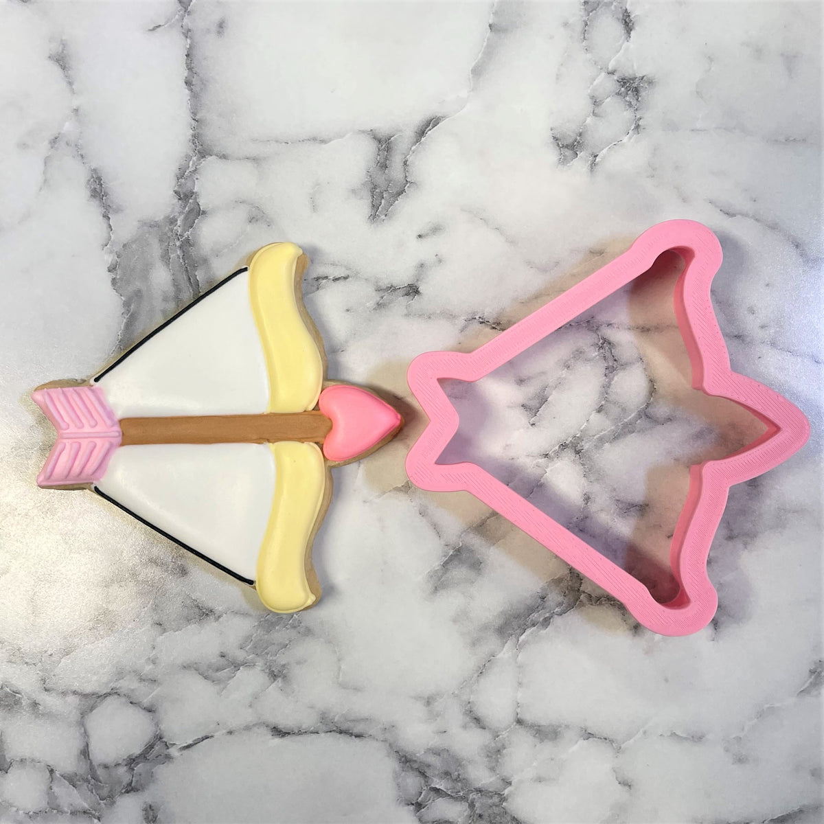 Pink star-shaped metal cookie cutter next to decorated arrow-themed cookie for bow and arrow baking fun