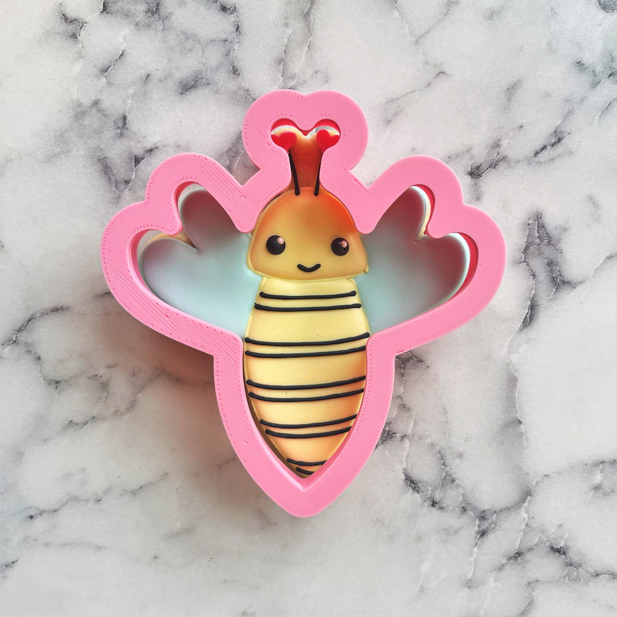 Bumblebee cookie cutter shaped like a pink plastic bee with yellow and black stripes and orange antennae