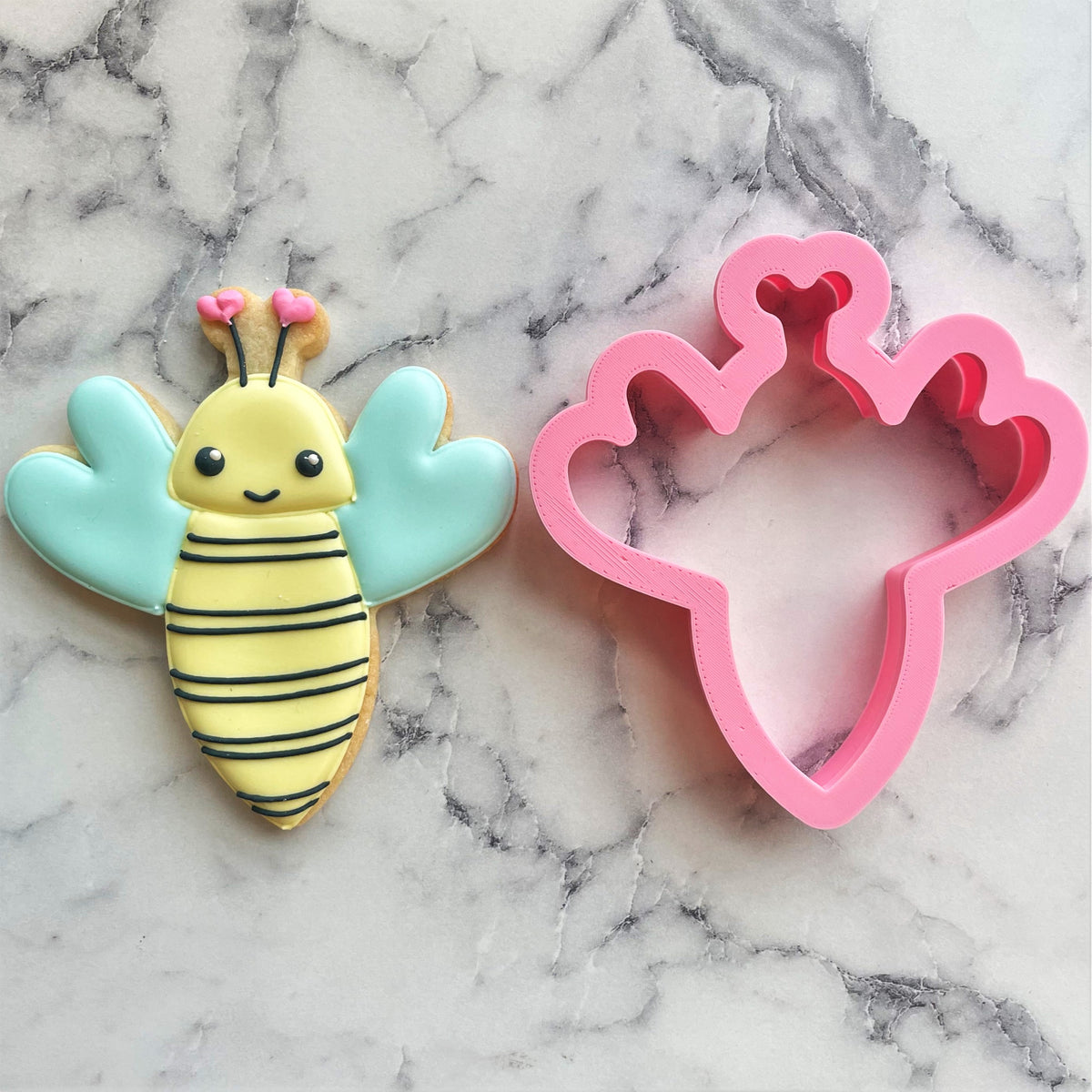 Pink plastic bumblebee cookie cutter with heart-shaped wings and antennae for baking and crafting