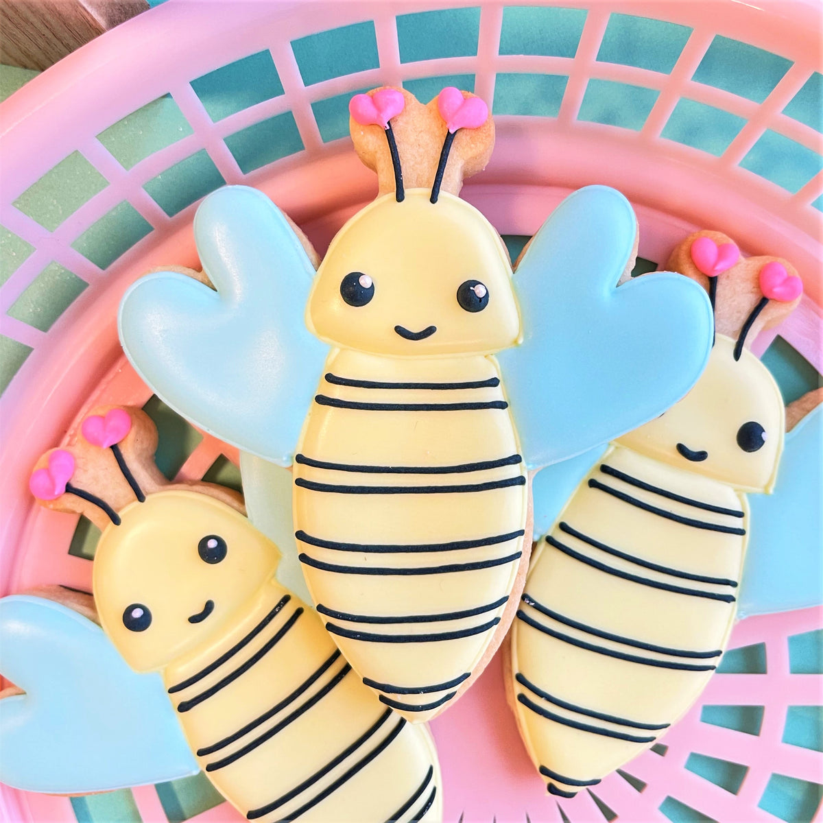Cute yellow and blue bee-shaped cookies with black stripes and pink antennae made using a bumblebee cookie cutter
