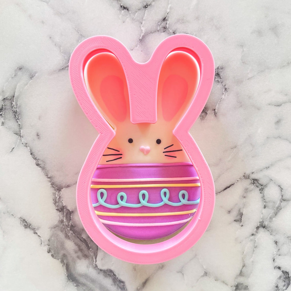 Pink bunny-shaped metal cookie cutter with striped purple and pink egg design inside for baking use
