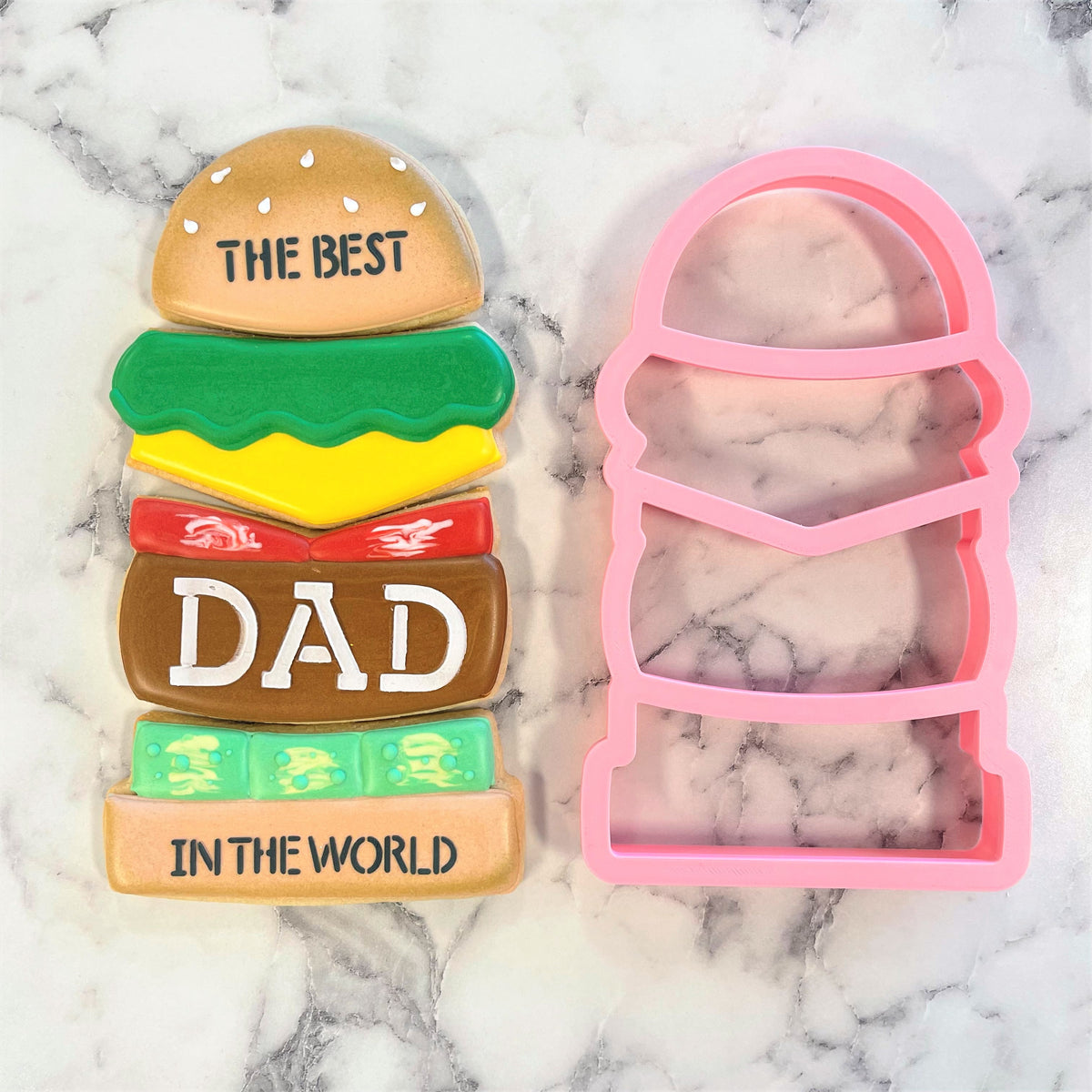 A colorful layered cookie shaped like a burger with the words the best dad in the world using burger stack 4-in-1 cookie cutter