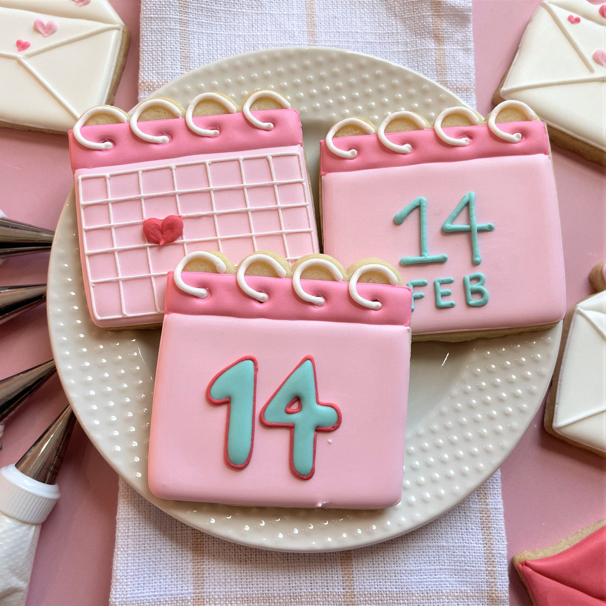 Pink frosted calendar cookies with teal numbers and white icing details made using a calendar cookie cutter