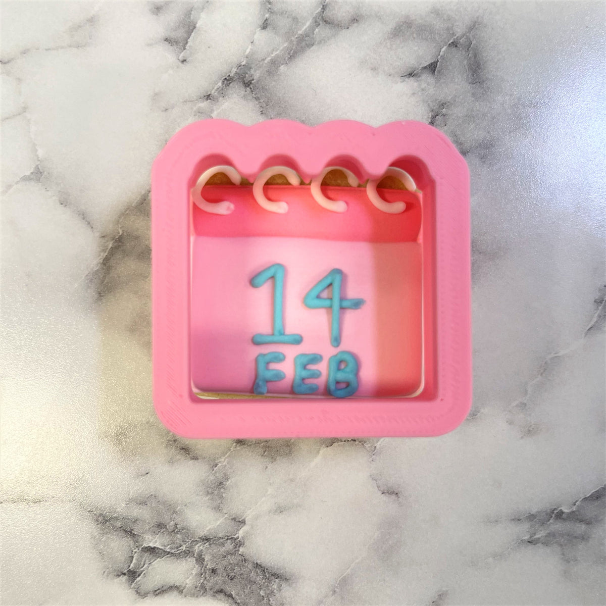 Pink silicone mini calendar cookie cutter mold with scalloped edges and blue embossed date 14 feb