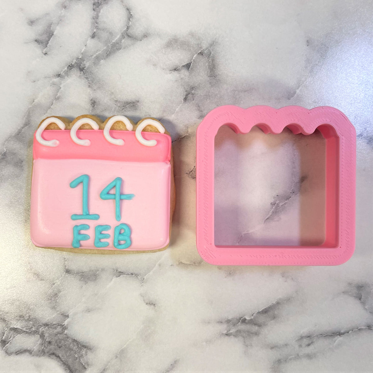Mini calendar cookie cutter with a pink silicone mold and a pink calendar-shaped cookie decorated with blue and white icing
