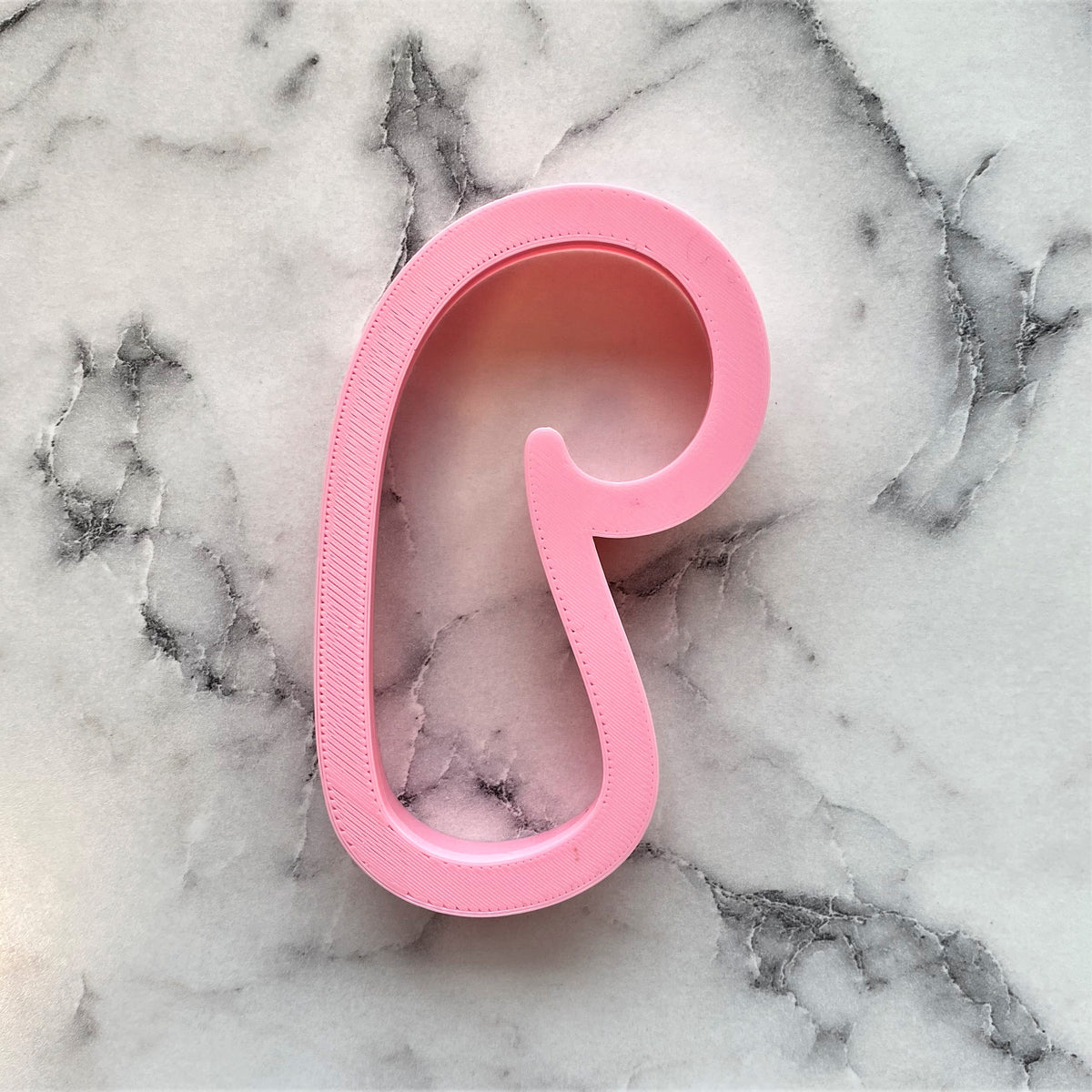 Pink plastic candy cane rounded cookie cutter with smooth rounded design and subtle textured edges for baking