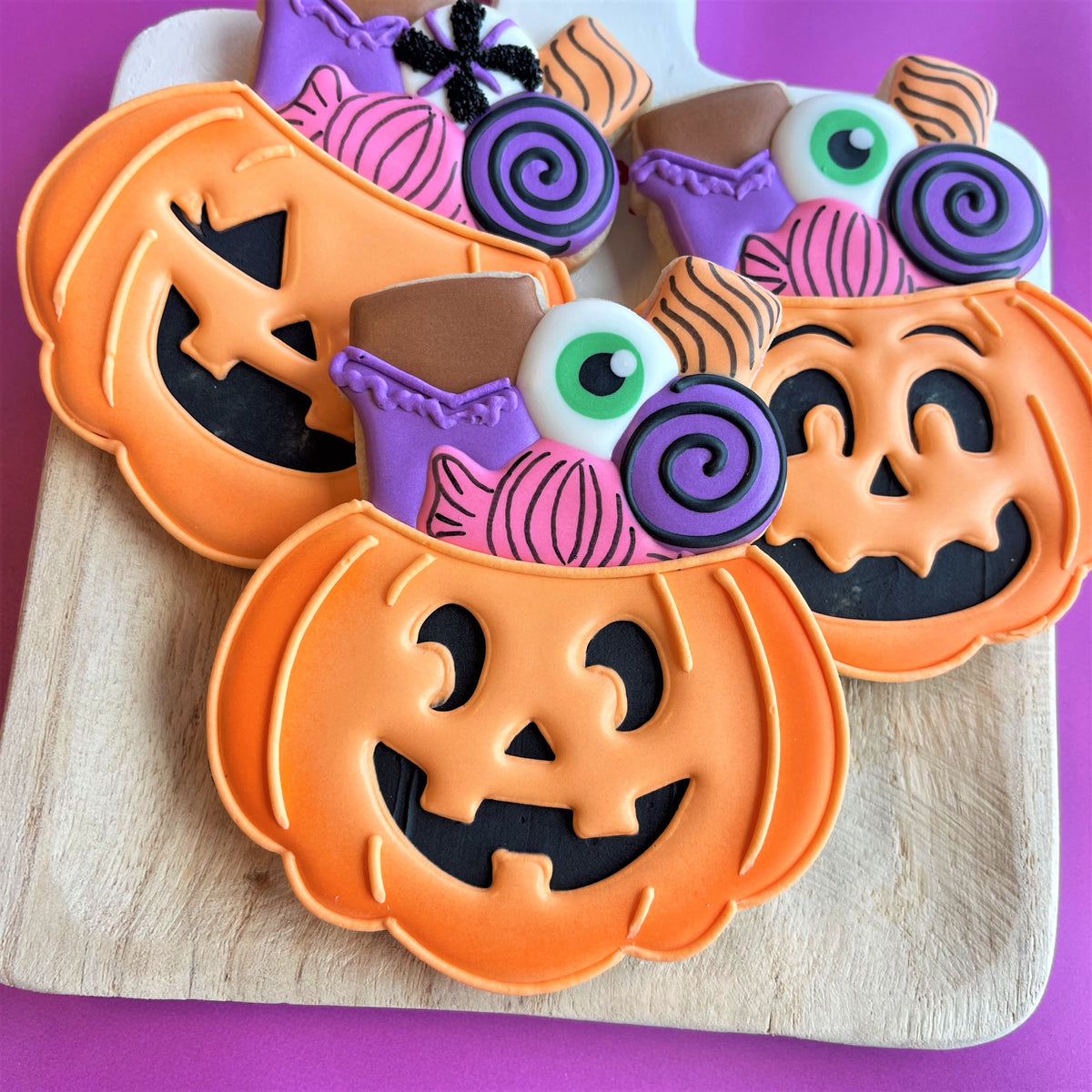 Orange pumpkin shaped cookies with black icing faces and colorful candy decorations from candy jack o lantern flour box club cookie cutter