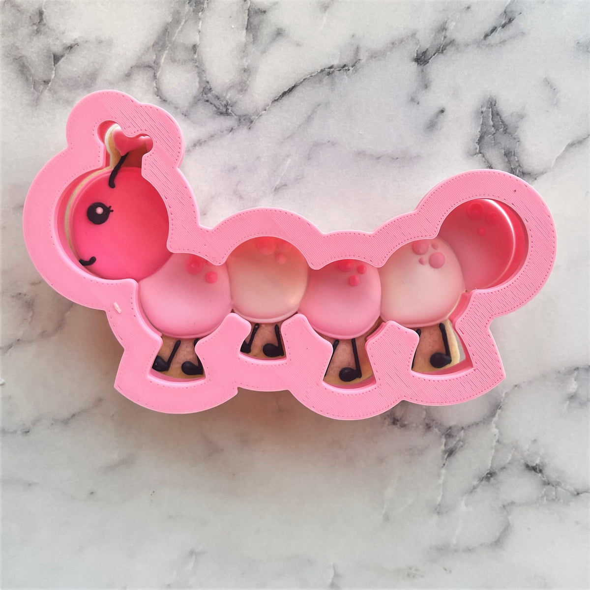 Pink plastic caterpillar cookie cutter shaped ice cube tray with segmented body and cute face for fun freezing