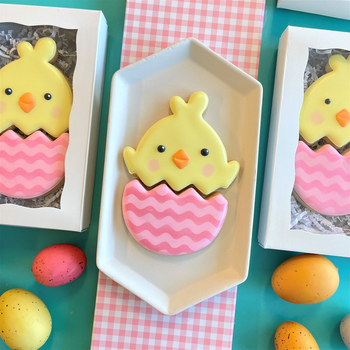 Yellow chick shaped cookie with black eyes orange beak and pink cheeks inside pink wavy eggshell cutter design