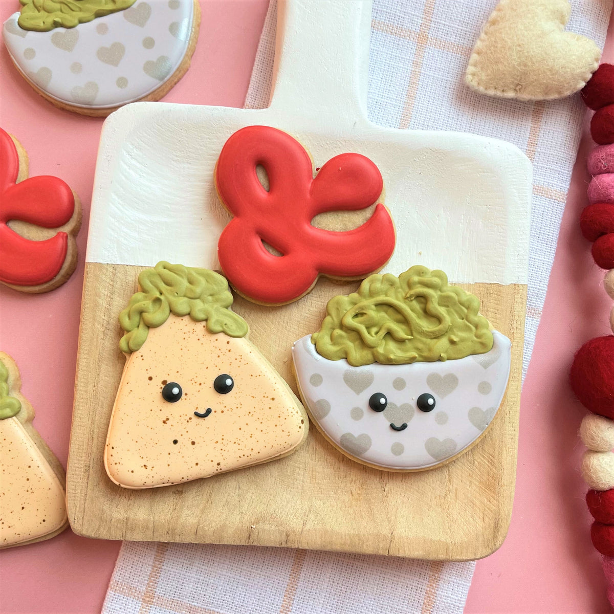 A charming guacamole cookie cutter shaped cookie with green icing and black dot eyes on a wooden cutting board