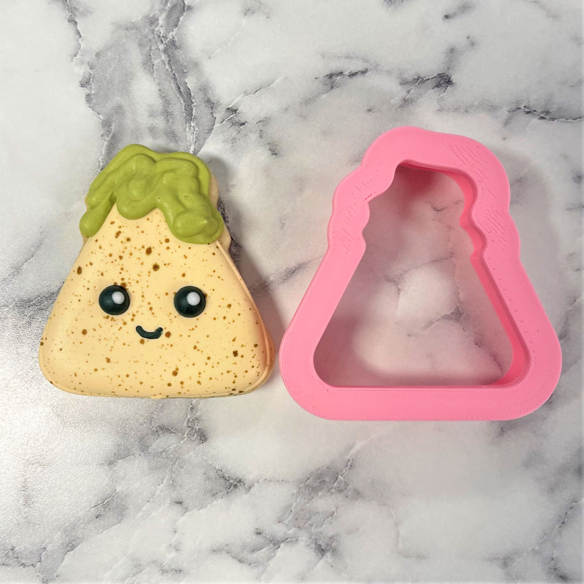 A pink silicone mini chip with guac cookie cutter and a yellow speckled taco stress reliever with a green top and smiling face