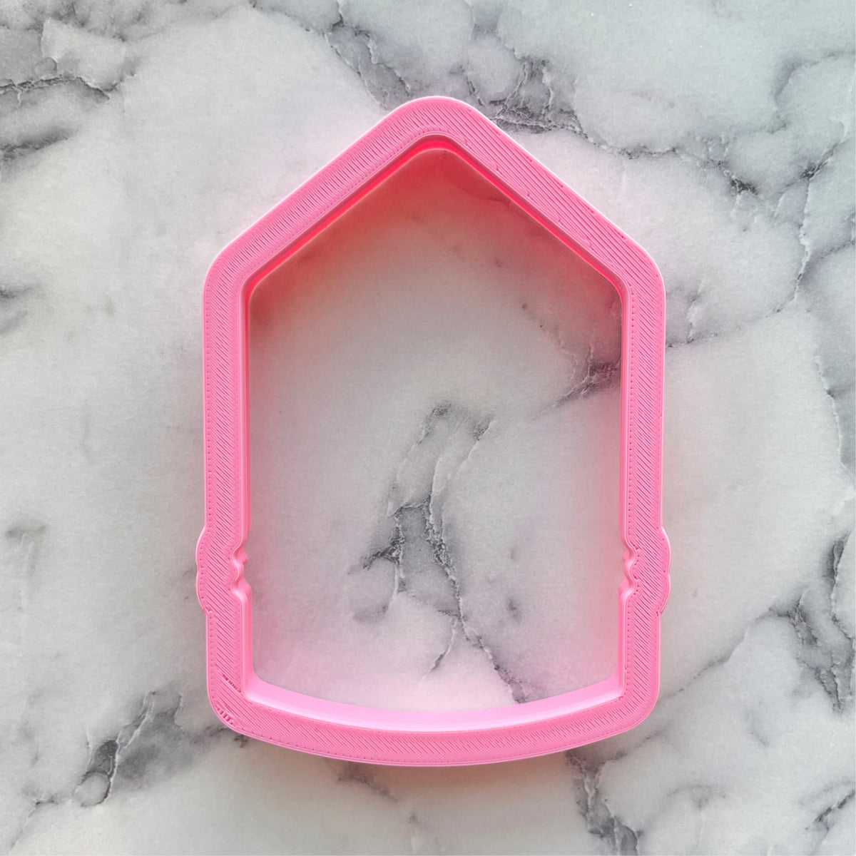 Pink plastic chubby XL pencil cookie cutter shaped like a house with textured layered edge and marble pattern interior
