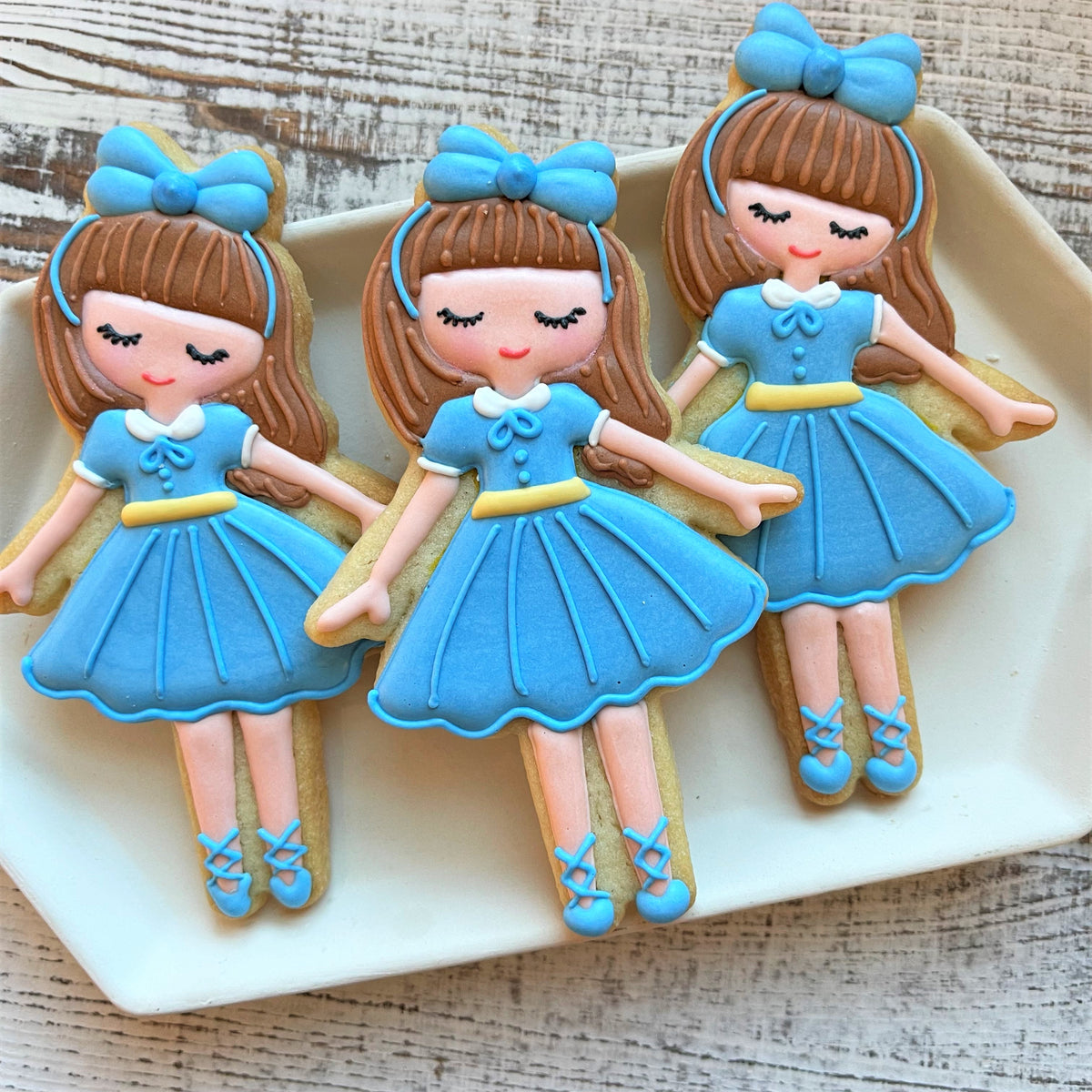Three blue ballet-themed sugar cookies decorated with detailed brown-haired dolls made using clara cookie cutter