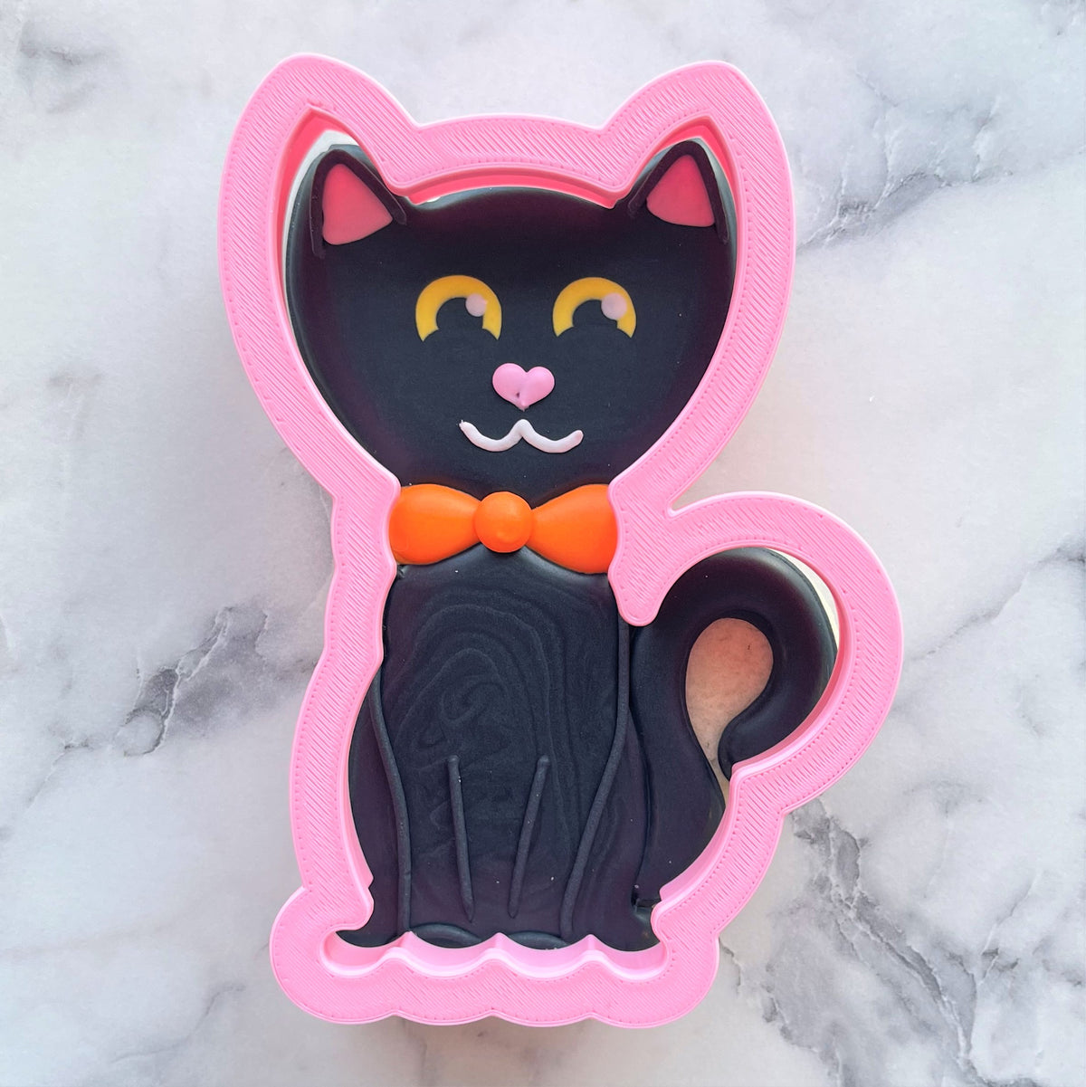 Pink silicone classic black cat cookie cutter with black fondant design featuring yellow eyes and an orange bow tie
