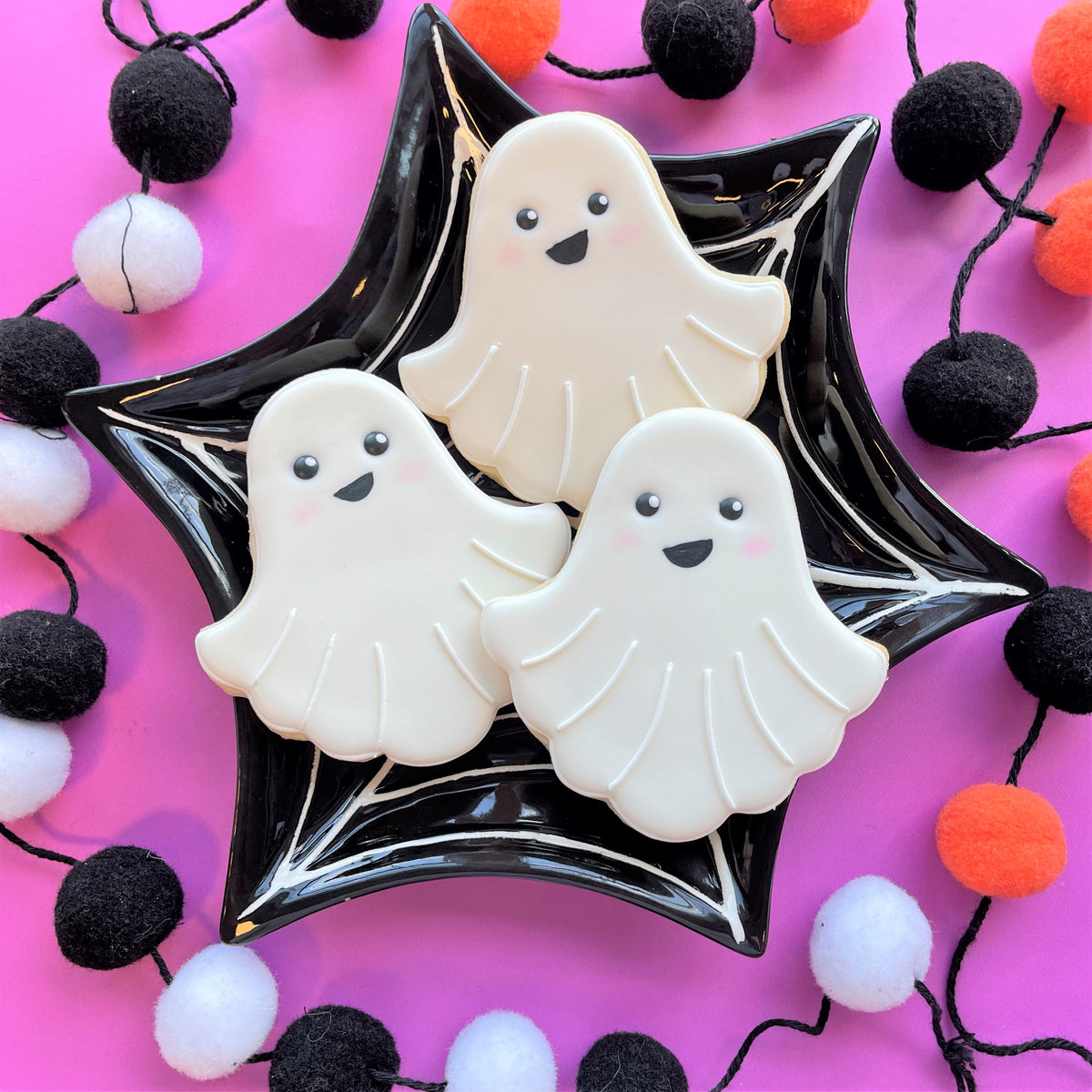 Classic ghost cookie cutter shaped white ghost cookies with black eyes and smiles on glossy black star plate